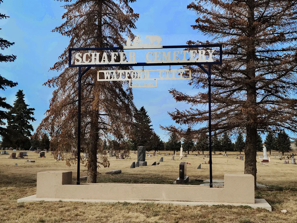 Entrance to Schafer Cemetery with its metal sign and graves in the grass.