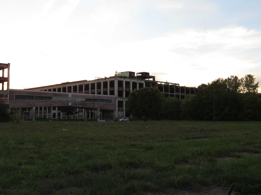 Old factory with large empty openings behind a meadow.