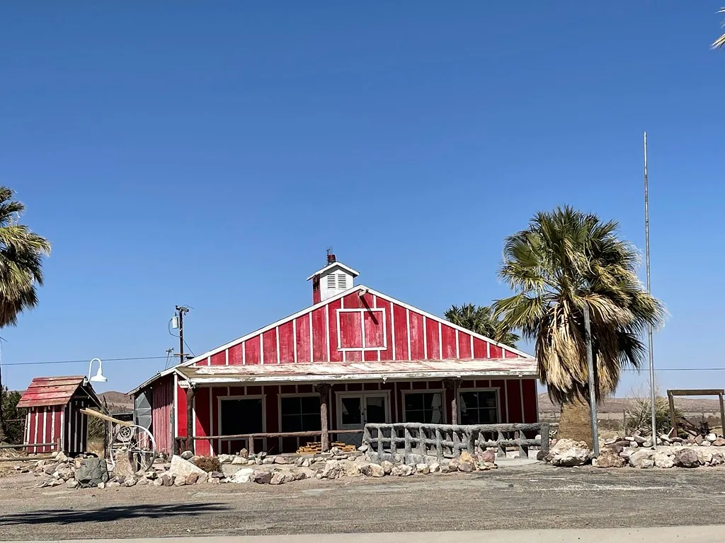 Abandoned red building with a dilapidated porch between palms and rocks.