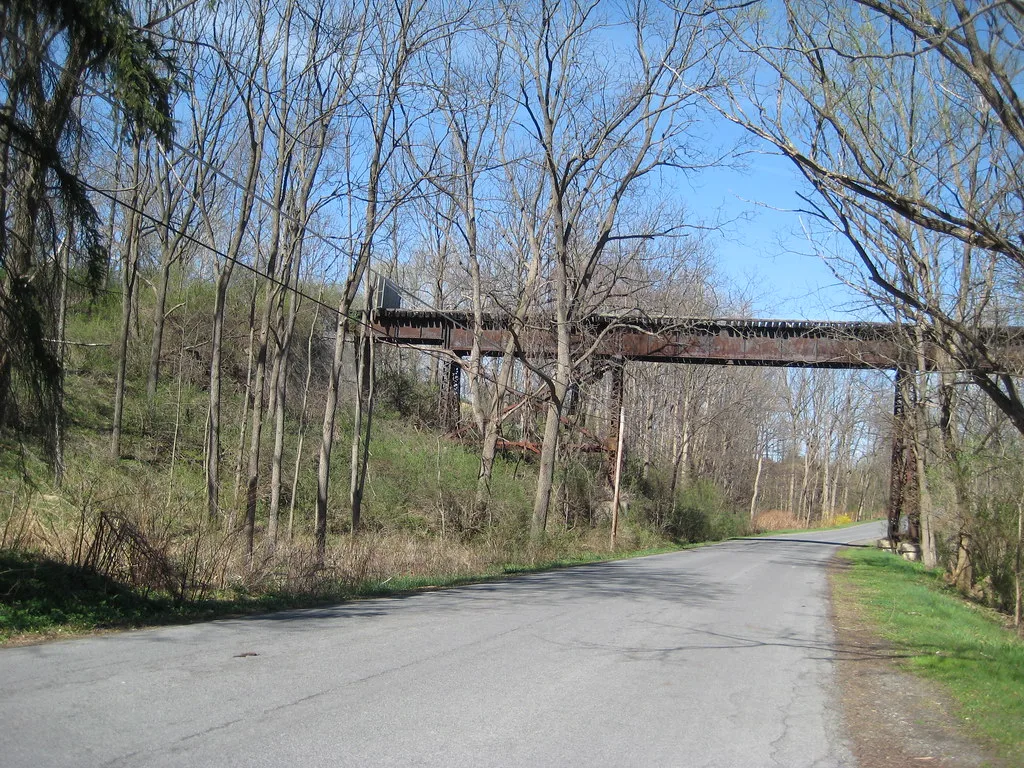 Ancien pont métallique rouillé parmi les arbres au-dessus d’une route.