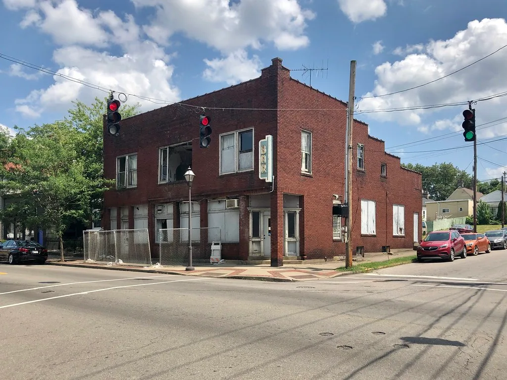 Abandoned red brick former bar with broken and boarded windows, a vertical sign and fencing around the entrance.