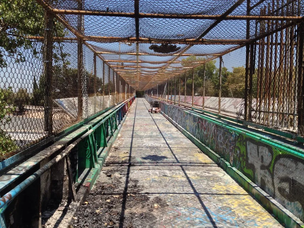 Passerelle grillagée couverte de graffitis au-dessus d’un canal.