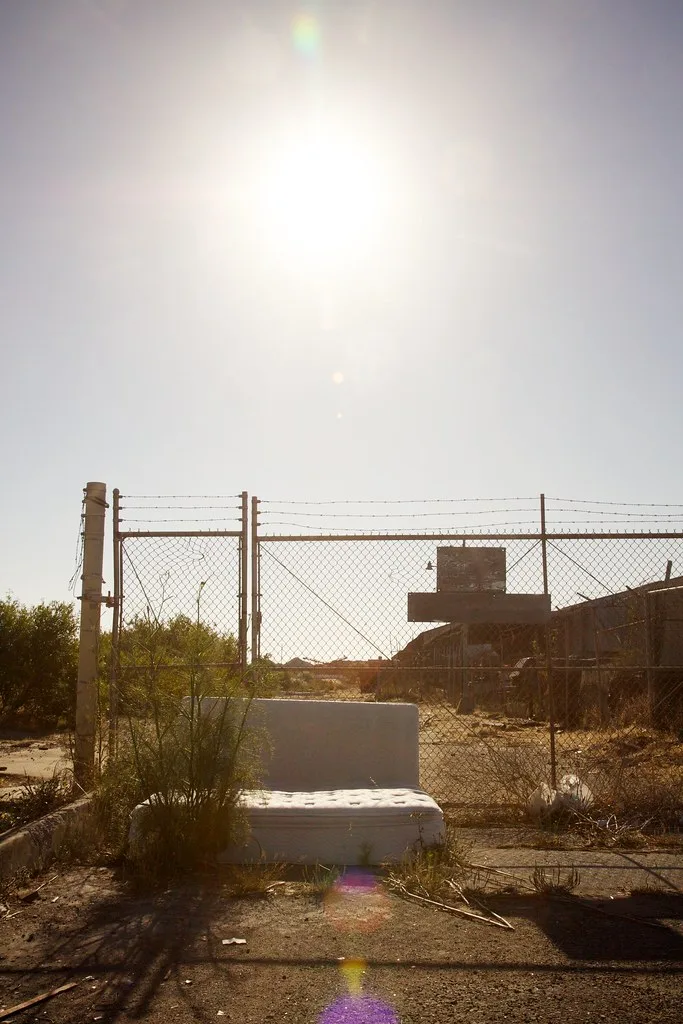 Ancien site industriel derrière une clôture avec un siège déposé au premier plan.