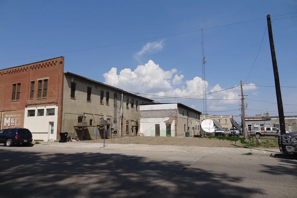 Old building with blocked openings and deteriorated facades beyond an empty lot.