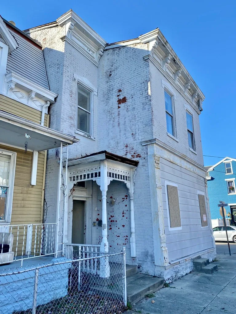 Old white building with boarded ground-floor openings and a deteriorated porch.