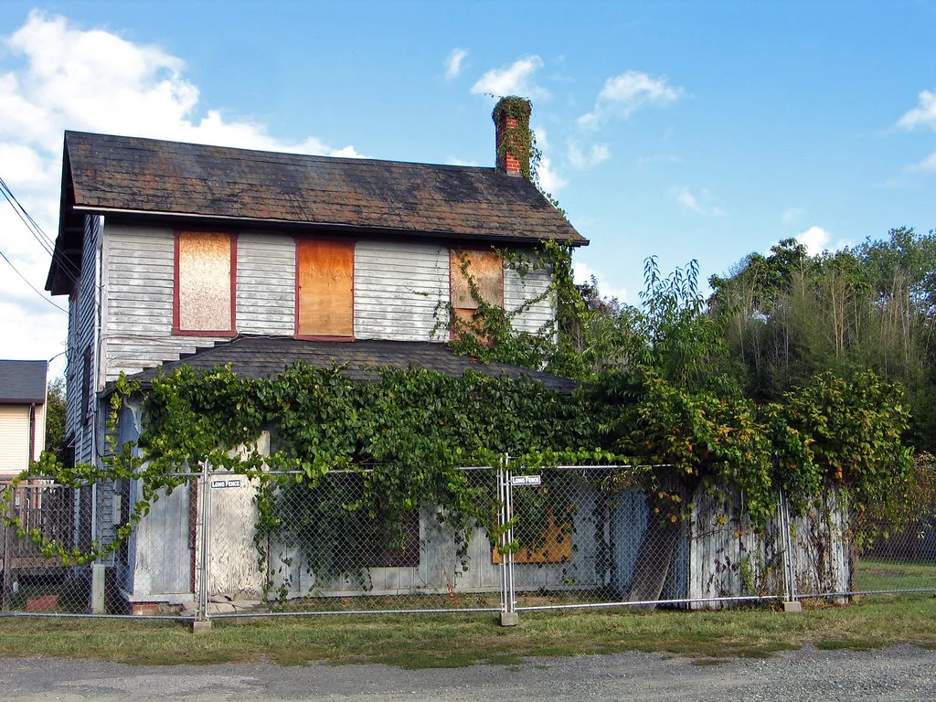 House with boarded windows behind a wire fence.