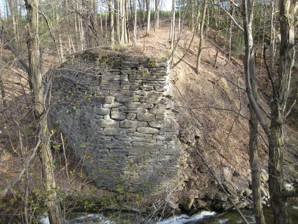 Old stone bridge abutment in woodland above a stream.