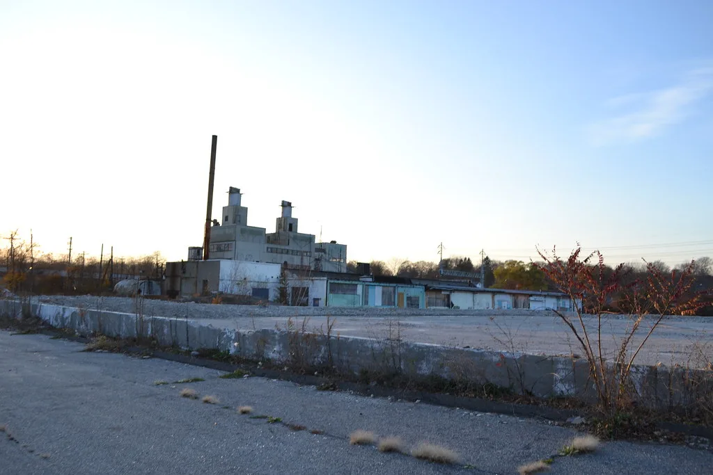 Old factory and concrete yard overgrown with weeds.
