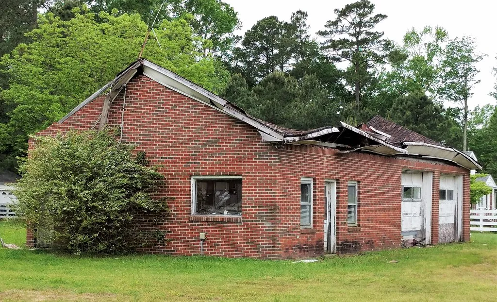 Ancien garage de briques au toit effondré au milieu d’une pelouse.