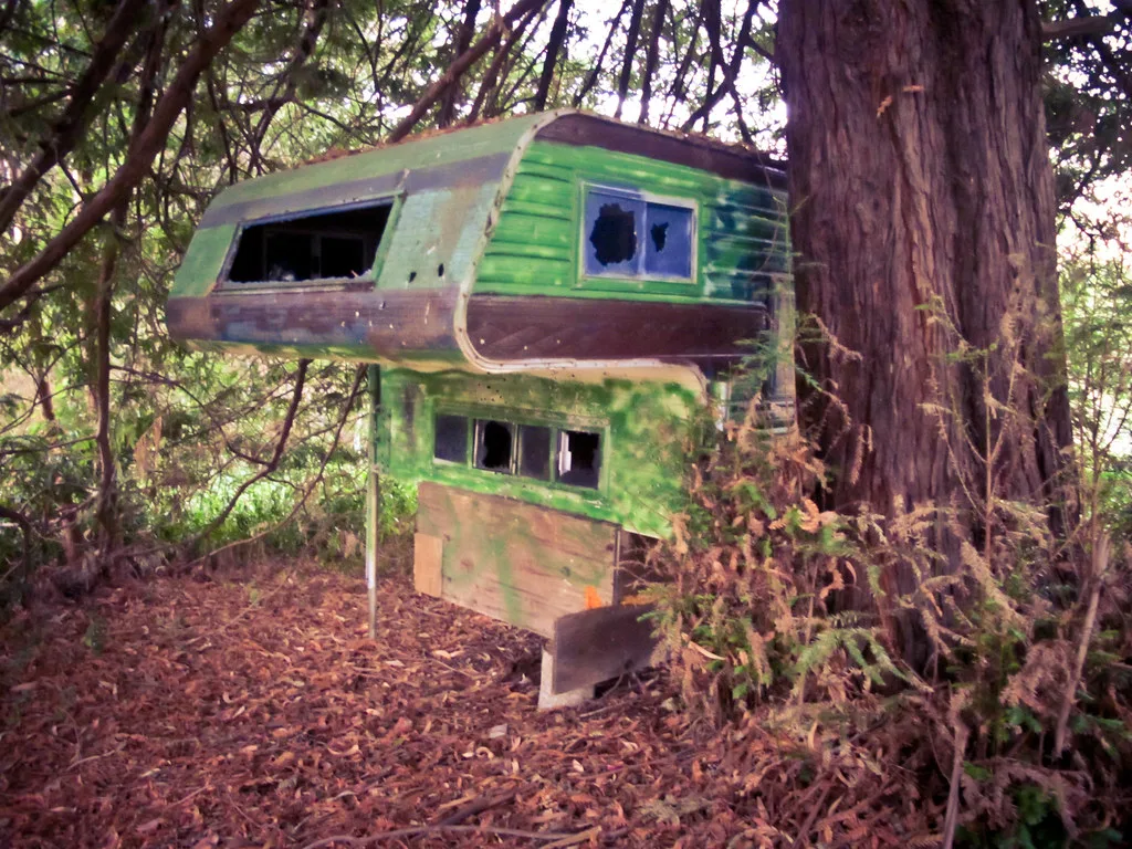 Old green camper shell with broken windows left in woodland.
