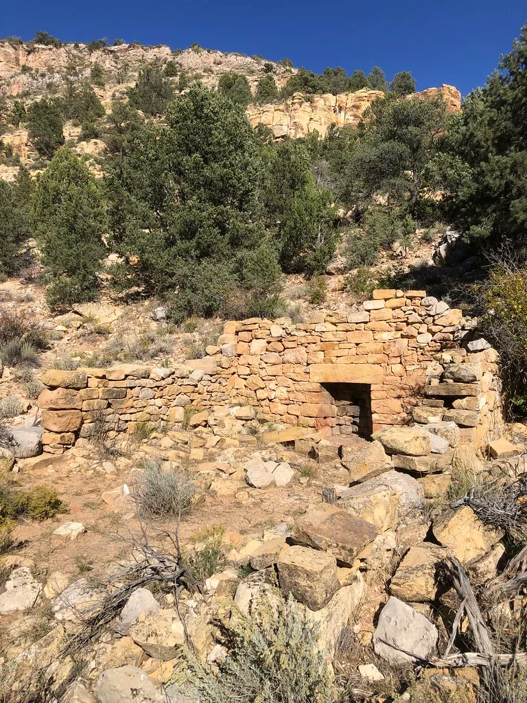 Ruined stone walls at the foot of a wooded rocky slope.