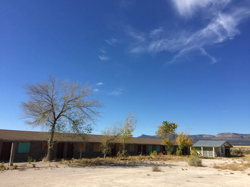 Old motel with boarded windows beyond an overgrown car park.