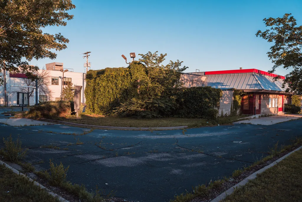 Former restaurant overgrown with ivy behind a cracked car park.