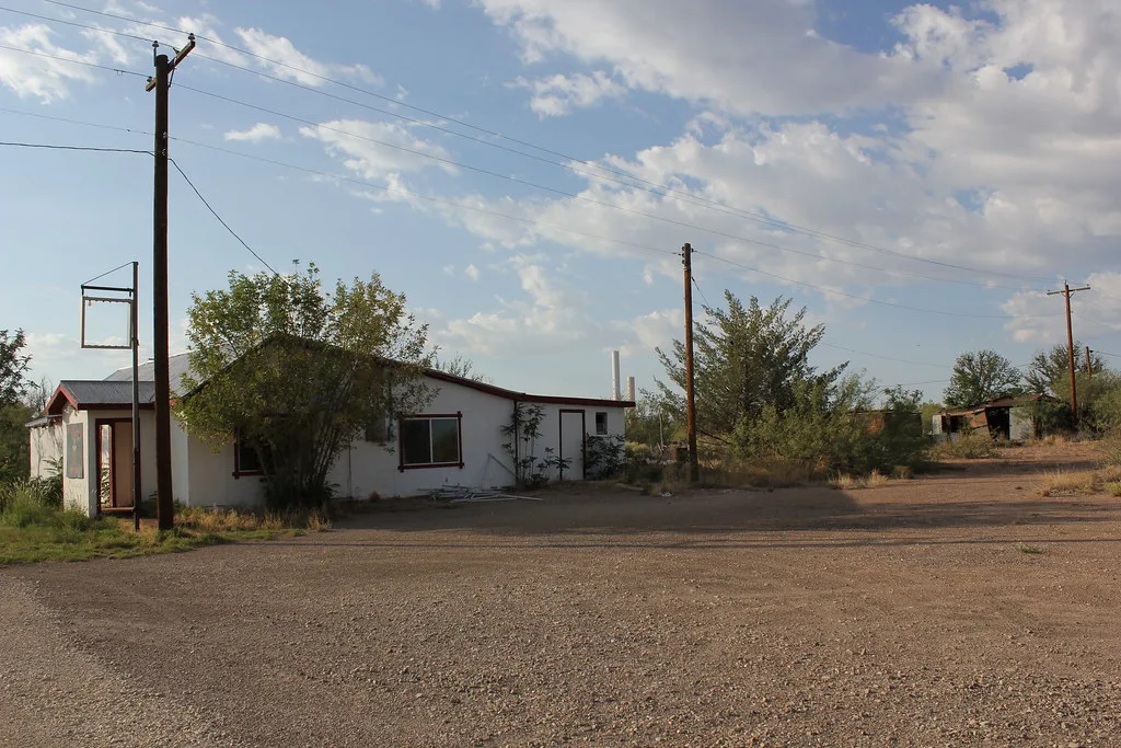 Derelict white commercial building with an open entrance and trees encroaching around it.