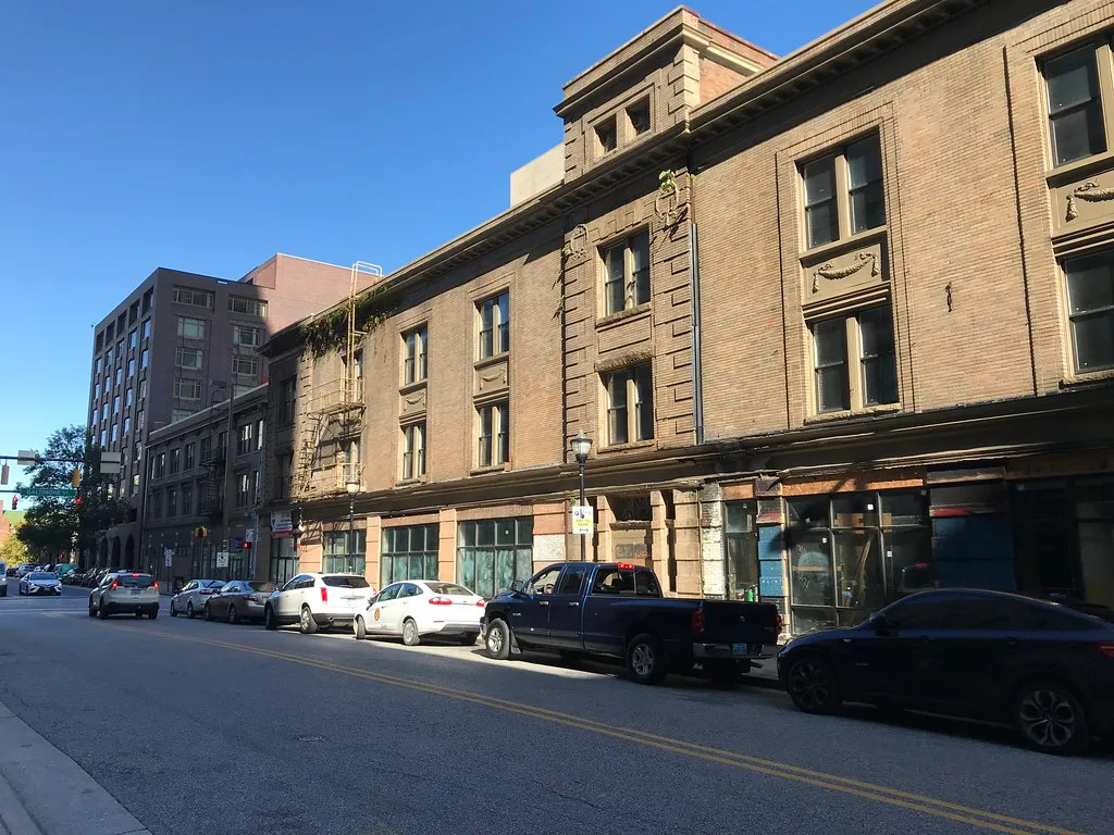 Old brick commercial building with damaged shop windows and vegetation on the cornice.