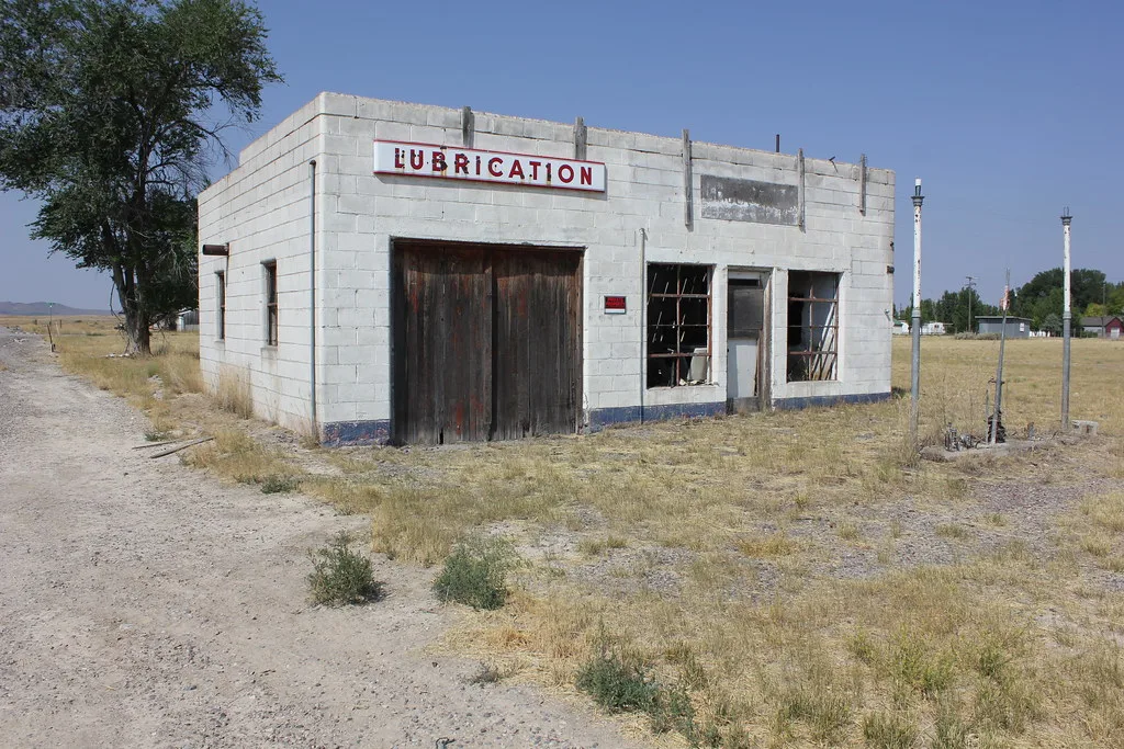 Old white garage with broken windows on a dry plot.