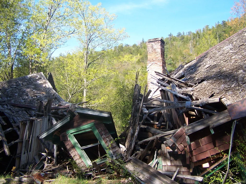 Collapsed wooden house around a brick chimney.