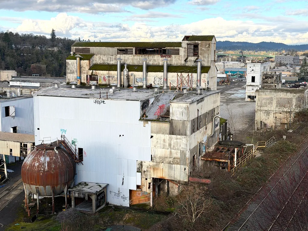 Deteriorated old industrial site with a rusty tank and moss-covered roofs.