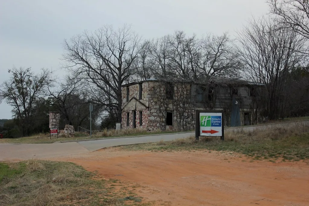 Abandoned stone and wooden building with gaping windows beyond a road.