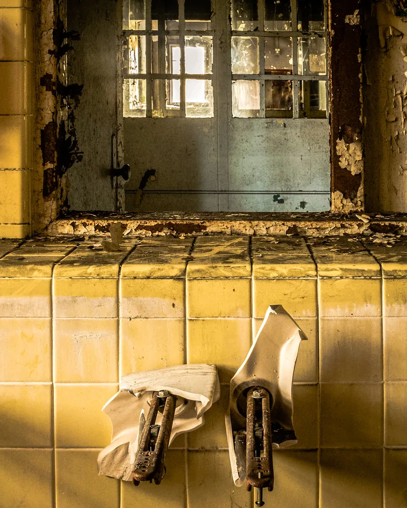 Lavabo brisé sous un miroir dans une salle d’eau délabrée.