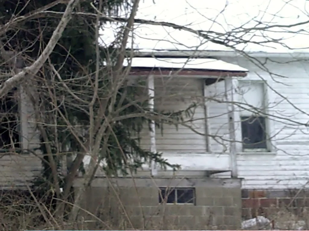 Old white house with a sealed porch behind bare branches.