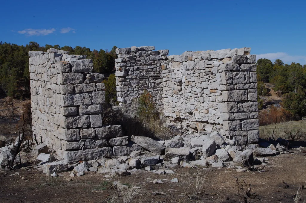 Ruins of a small grey stone room with fallen blocks before an opening.