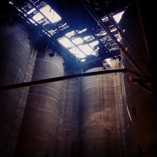 Silos en béton sous une charpente et une toiture percée.