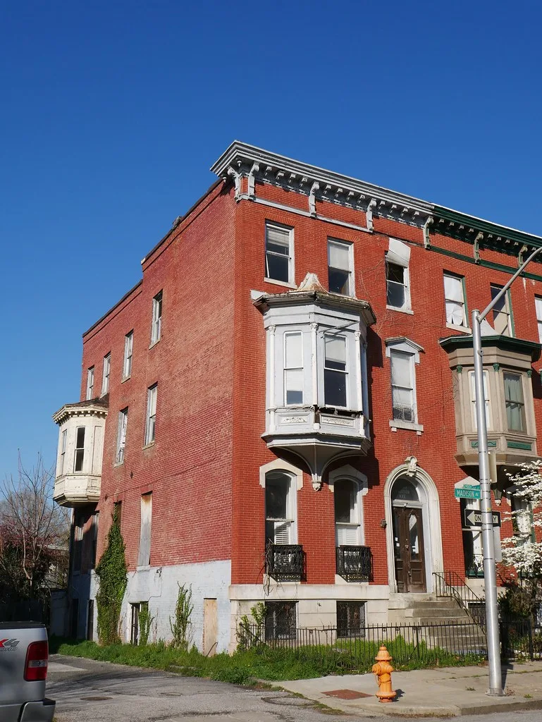 Old red-brick house with deteriorated white bay windows and broken glass.