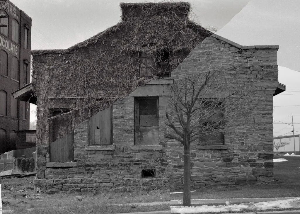 Ancien bâtiment de pierre condamné et couvert de lianes, en noir et blanc.