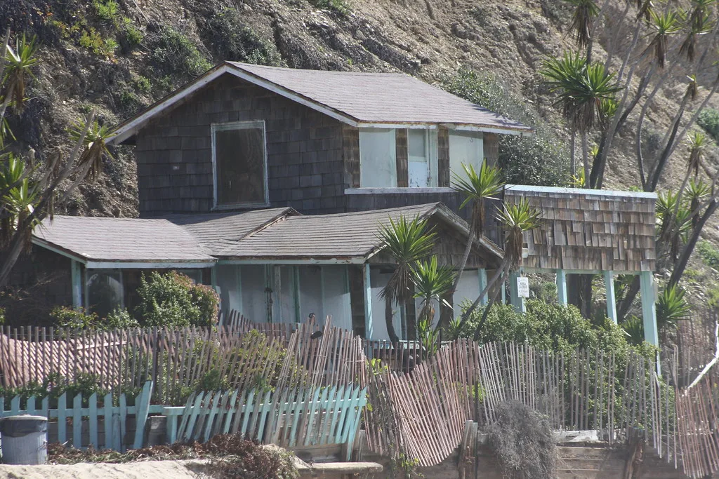 Old wooden house with boarded openings behind leaning fences.