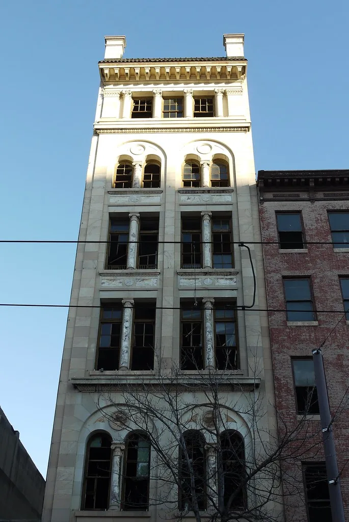 Old narrow pale-fronted building with broken windows.