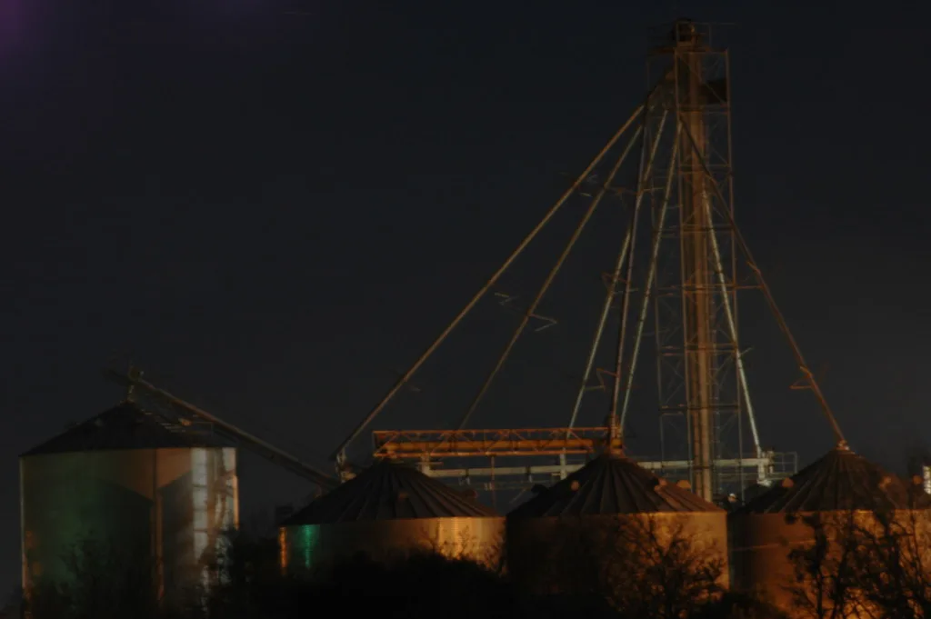 Old rusty silos and a metal tower photographed at night.