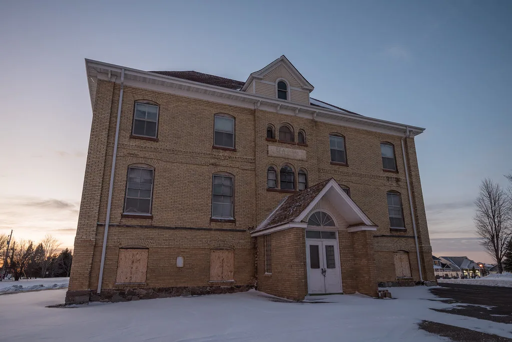 Old yellow brick building with boarded lower windows in the snow.