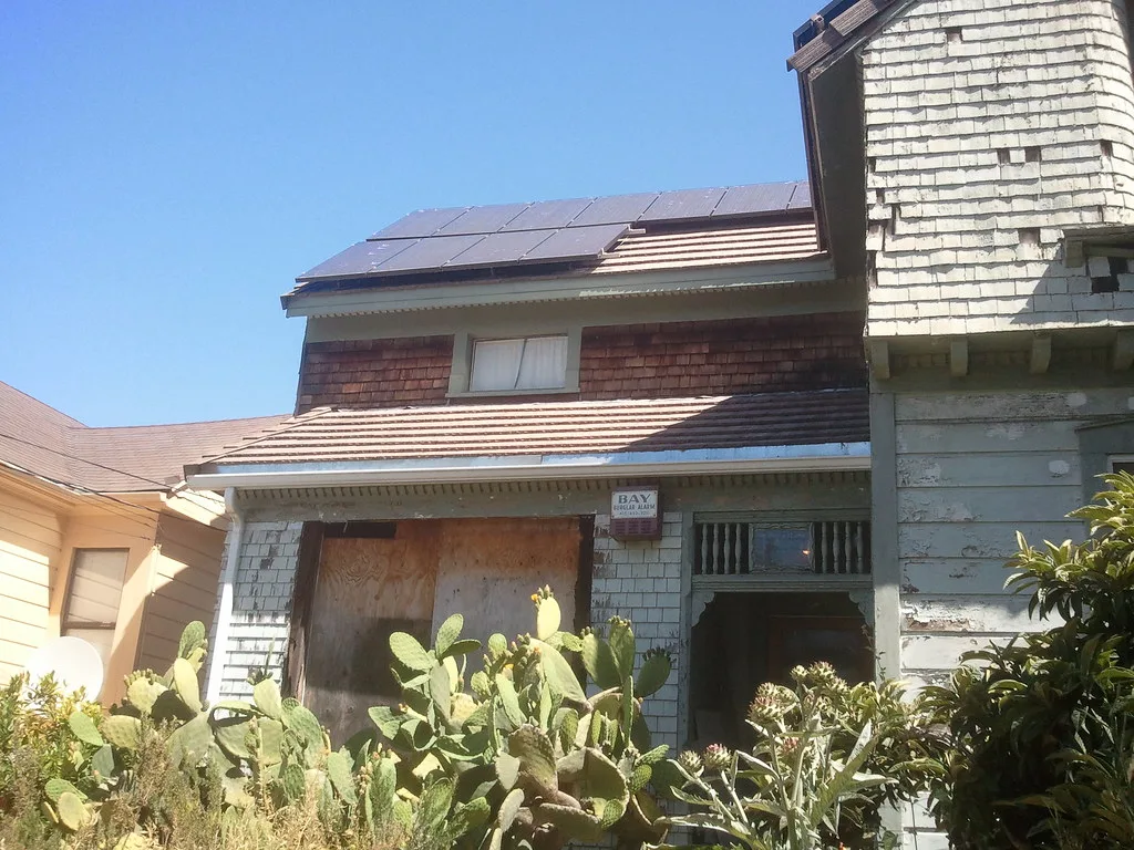 Ancienne maison aux fenêtres condamnées envahie de cactus.