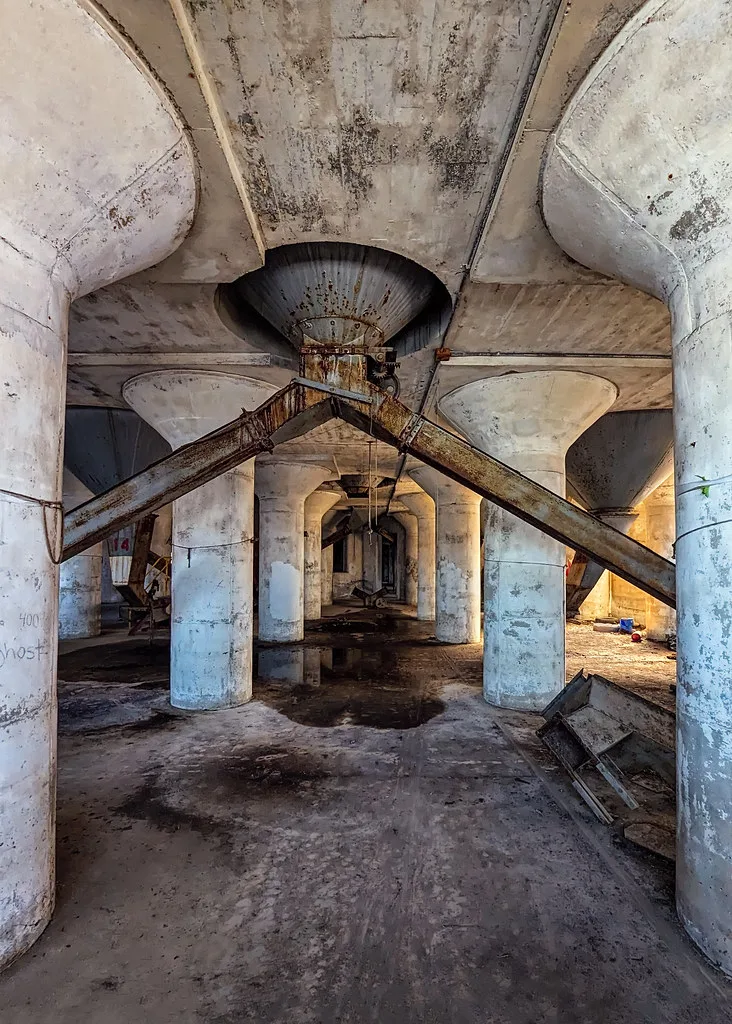 Row of pillars and rusty hoppers inside an old industrial building.