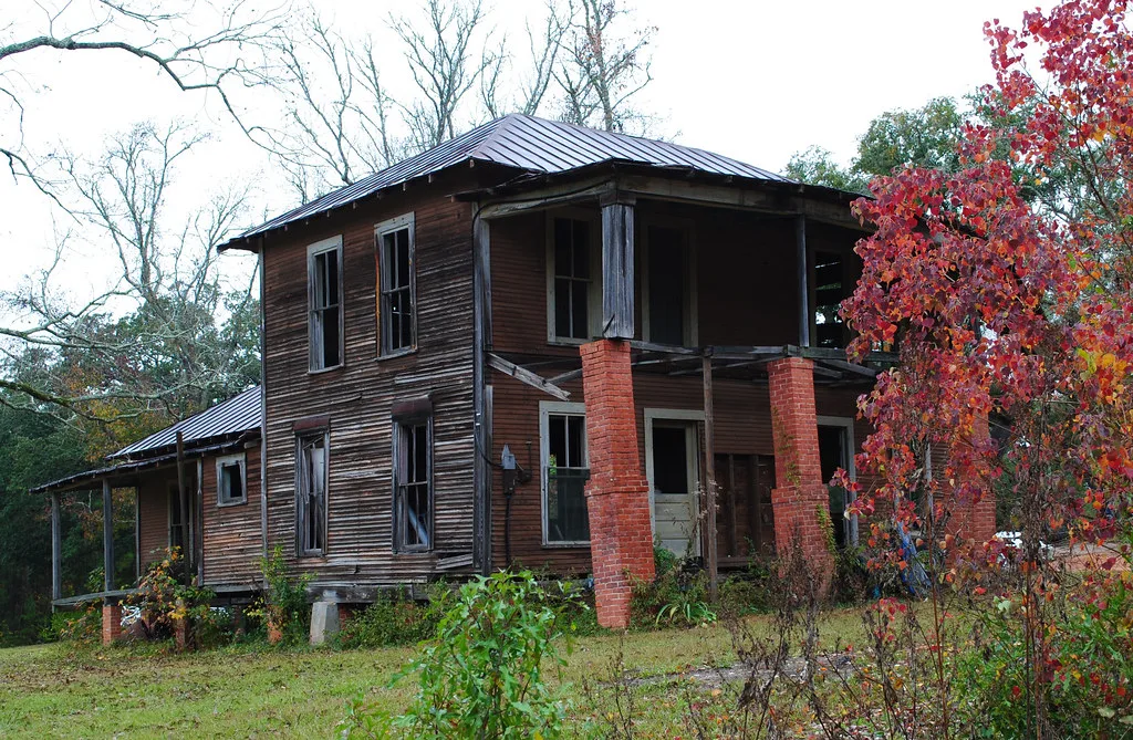 Old wooden house with empty windows and a deteriorated porch.