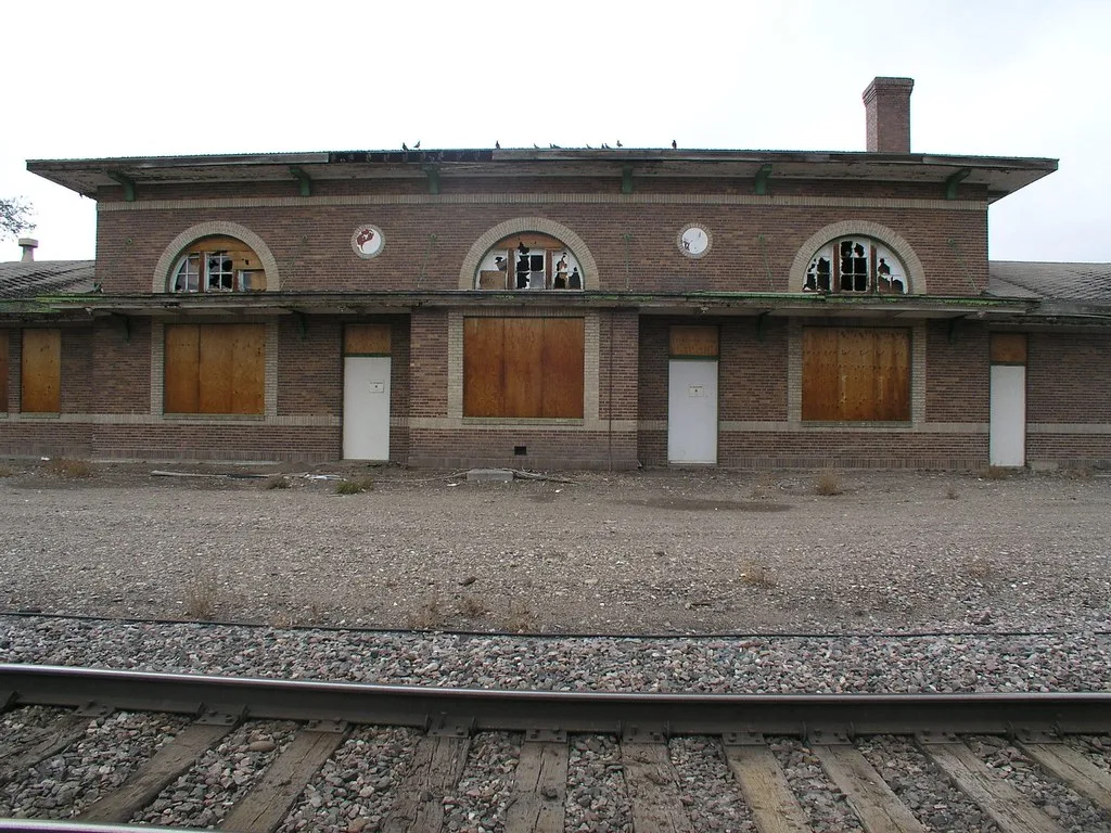 Brick station facade with broken arched windows and boarded openings.