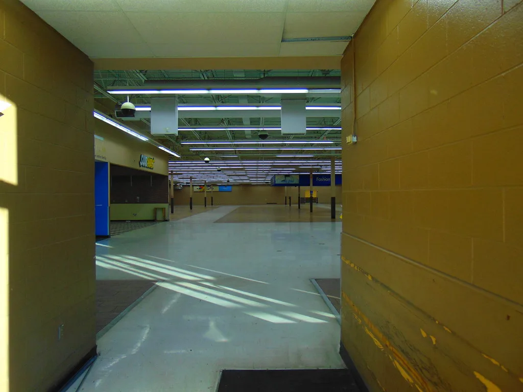 Empty interior of a former store beneath rows of lights.