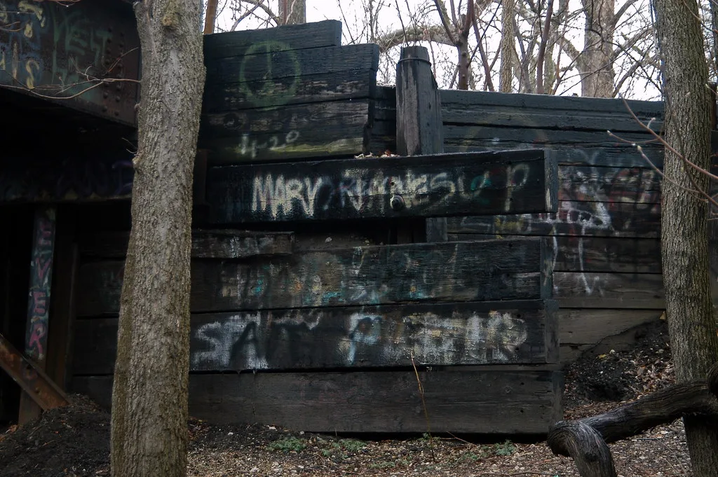 Old structure of graffiti-covered timber beams among trees.