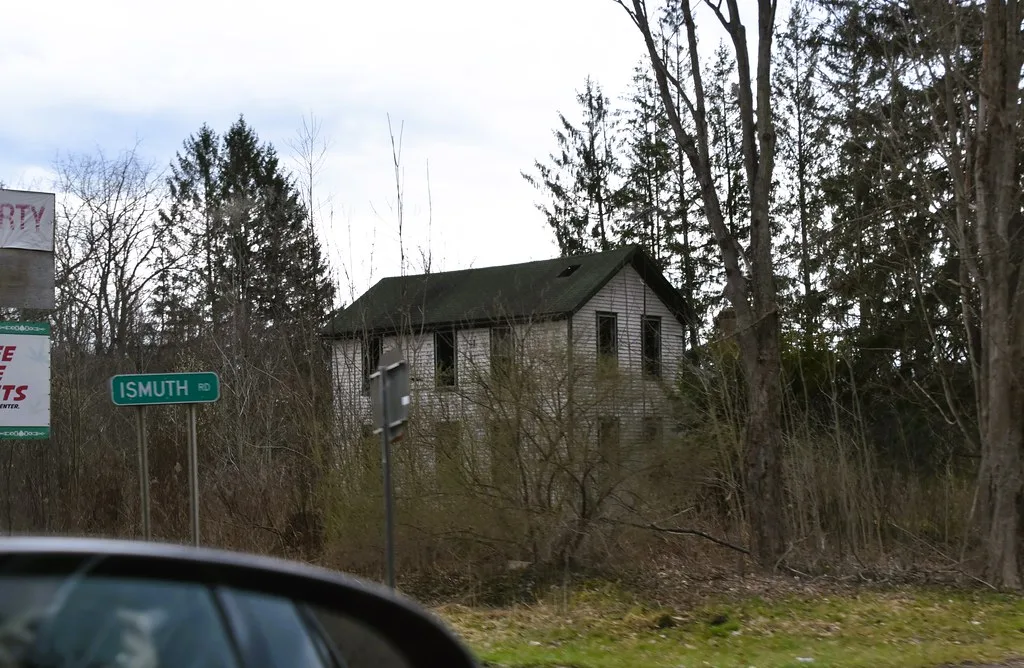 Maison abandonnée aux ouvertures vides derrière les broussailles.