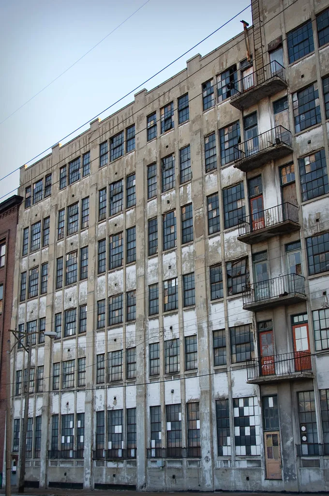 Abandoned facade of a large industrial building with broken or blocked windows and stacked metal balconies.