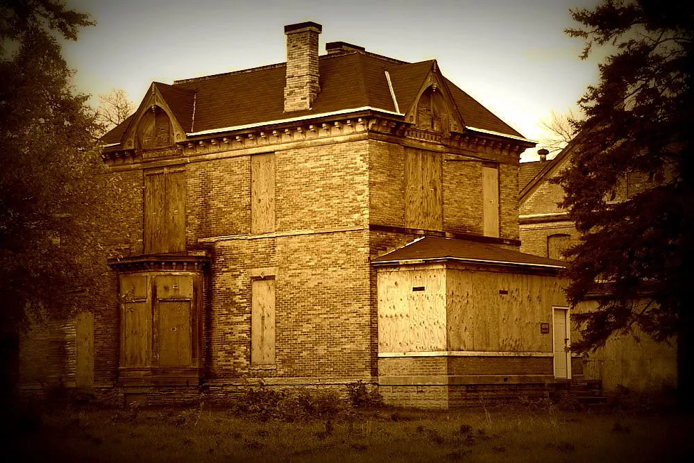 Brick house with a dark roof and all openings sealed with wooden boards.