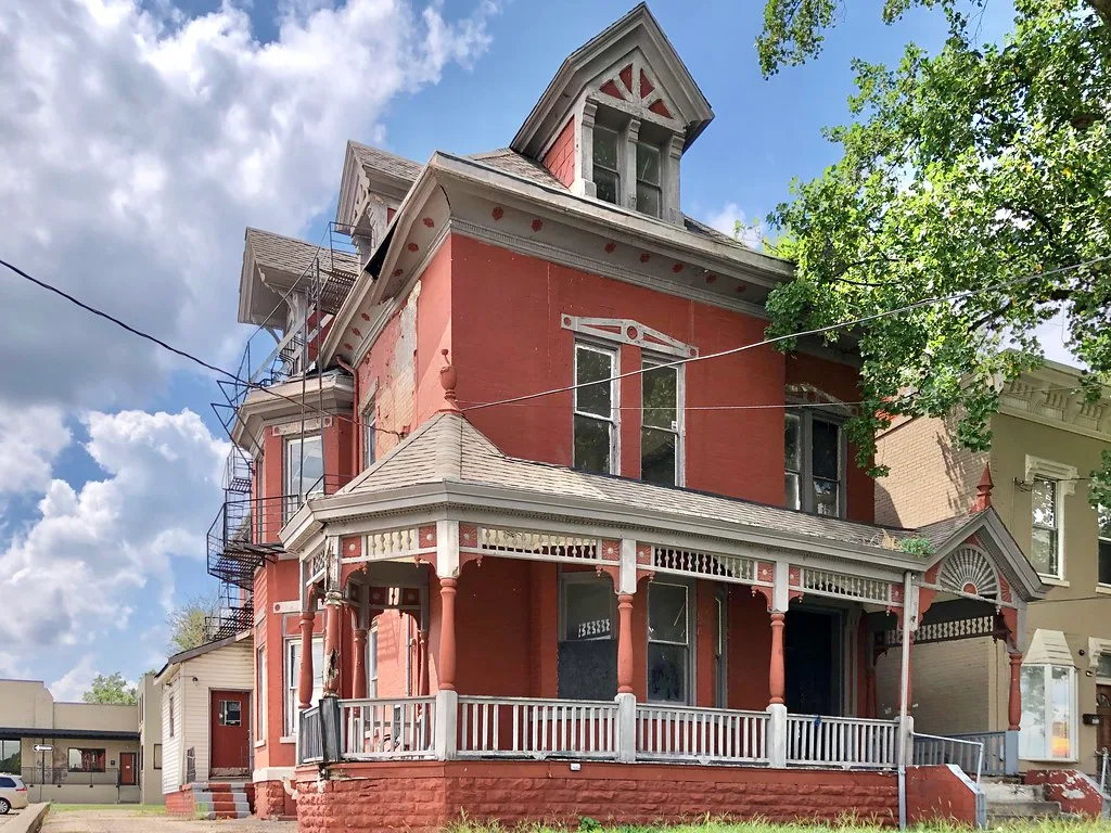 Old red house with broken windows and boarded entrances.