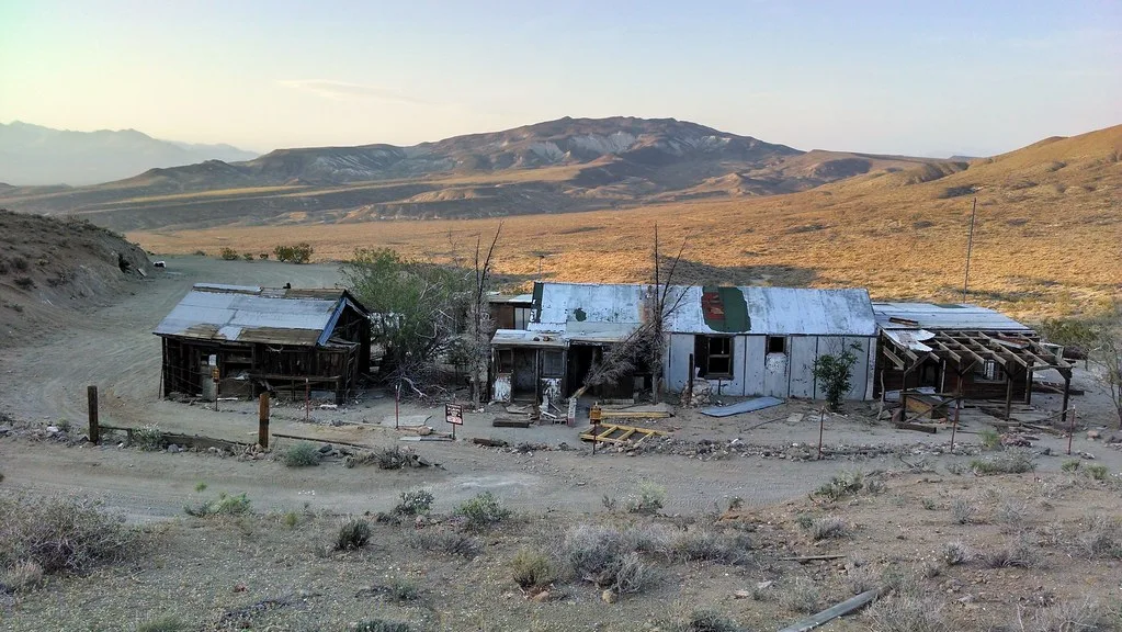 Baraques abandonnées aux toitures éventrées dans un paysage désertique de collines.