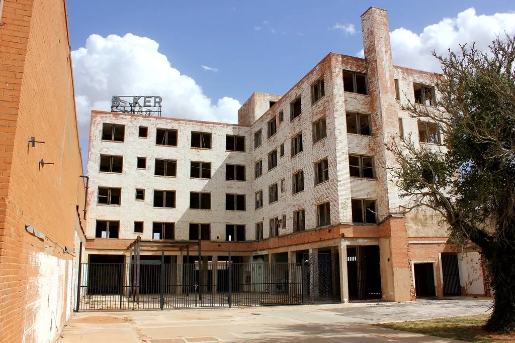 Courtyard of a large abandoned building with five floors of empty windows behind a black gate.