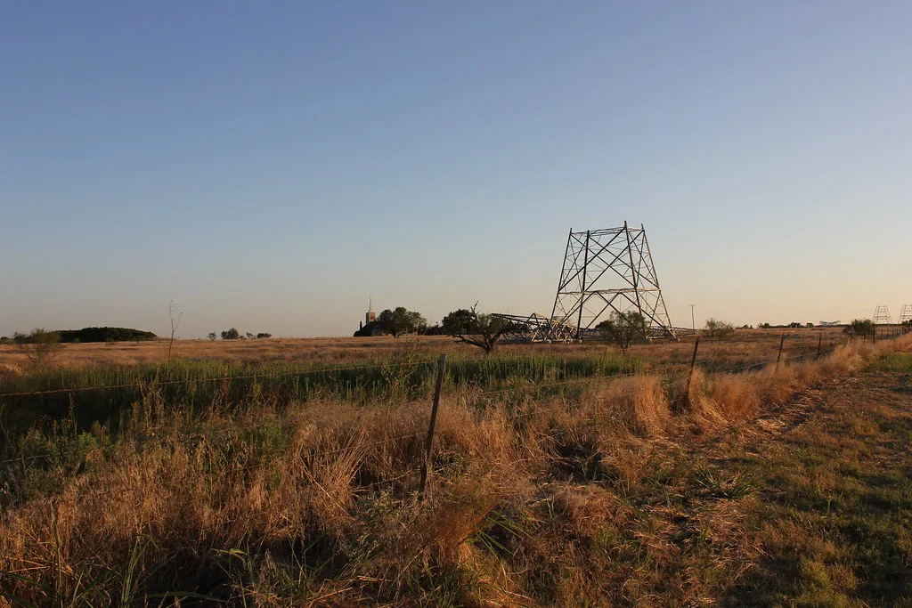 Remains of a metal tower and collapsed framework in a dry meadow.