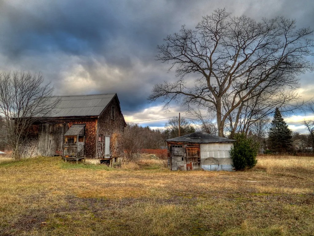 Weathered old barn and small shed in a meadow beneath a dark sky.