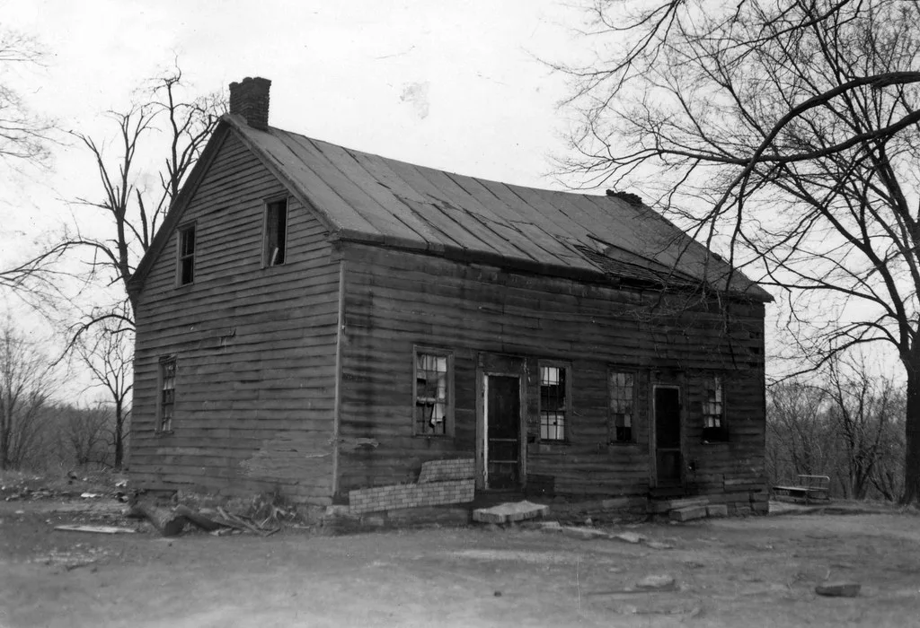 Ancienne maison de bois aux fenêtres brisées, en noir et blanc.