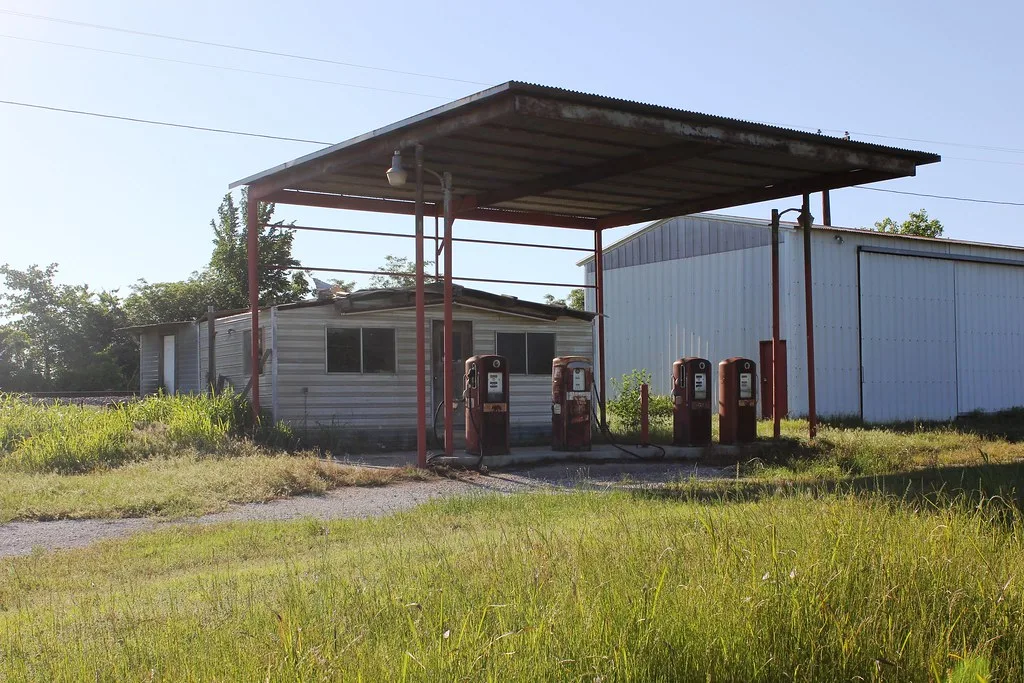 Ancienne station-service aux pompes rouges rouillées dans les hautes herbes.