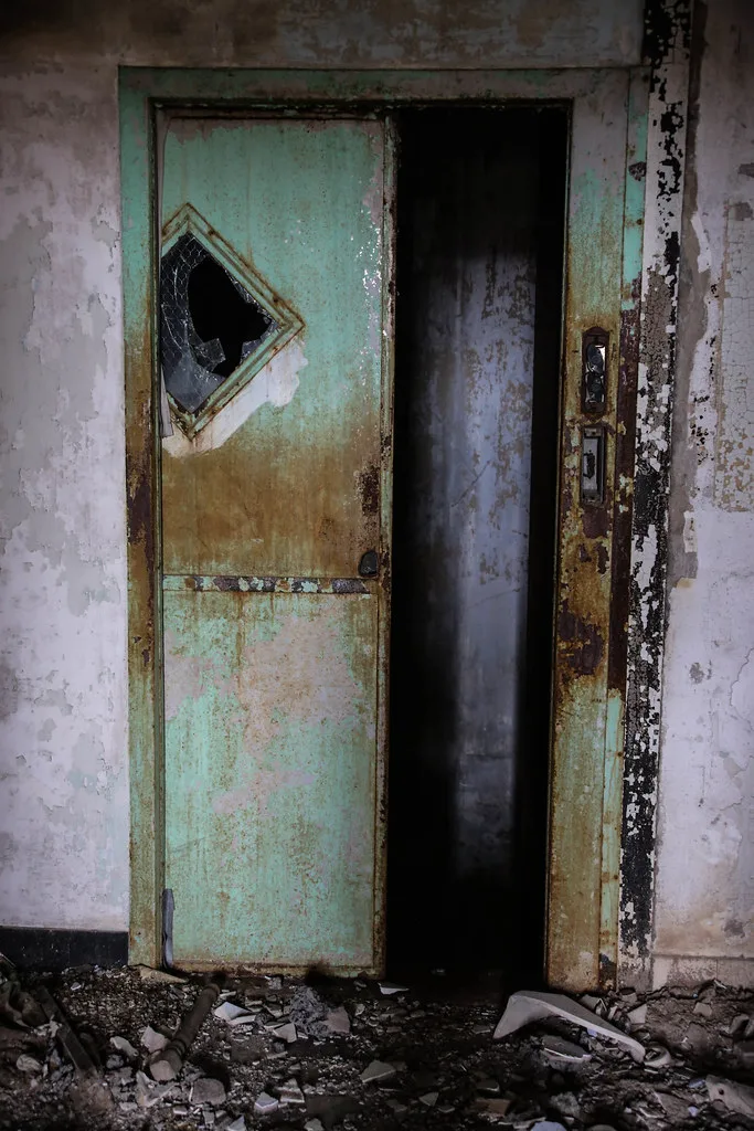 Old green rusted lift door amid peeling walls.